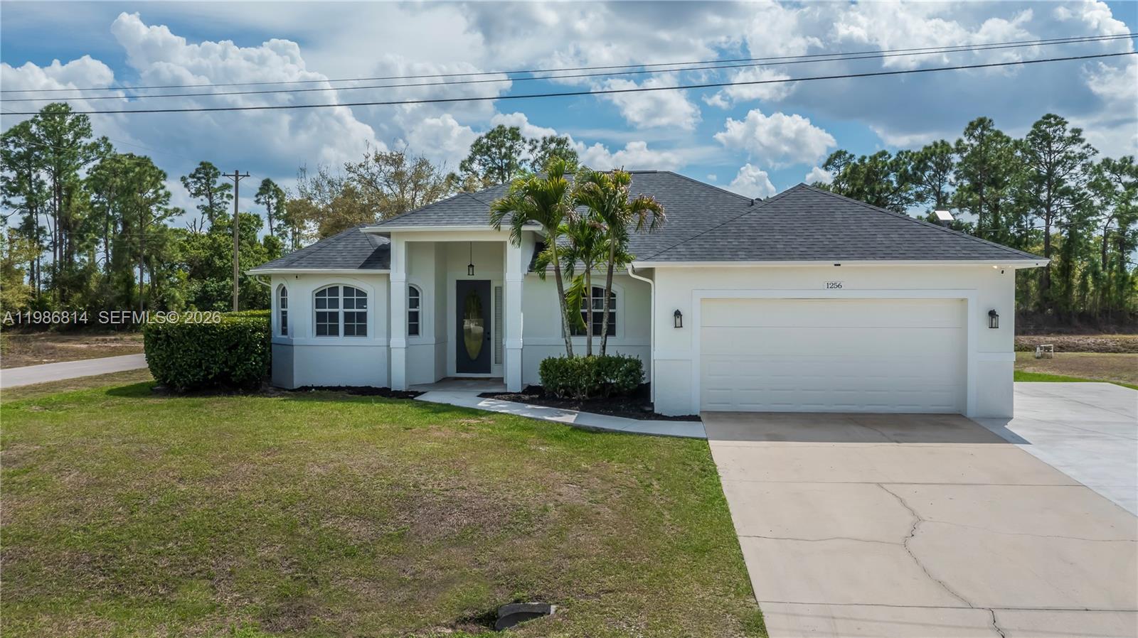 A single-story white house with a dark shingled roof and a two-car garage — 1256 E Edna St., Lehigh Acres FL 33974, LEHIGH ACRES, FL