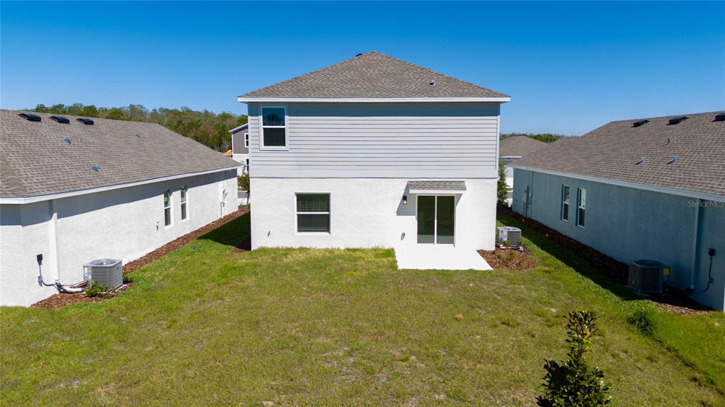 The rear exterior of a two-story house features a small concrete patio and lawn — 5858 LE MARIN WAY, KISSIMMEE, FL