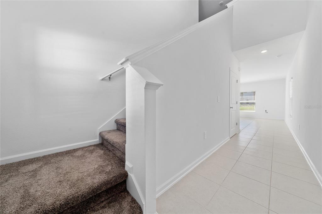 A carpeted staircase leads upward next to a tiled hallway with white walls — 5858 LE MARIN WAY, KISSIMMEE, FL