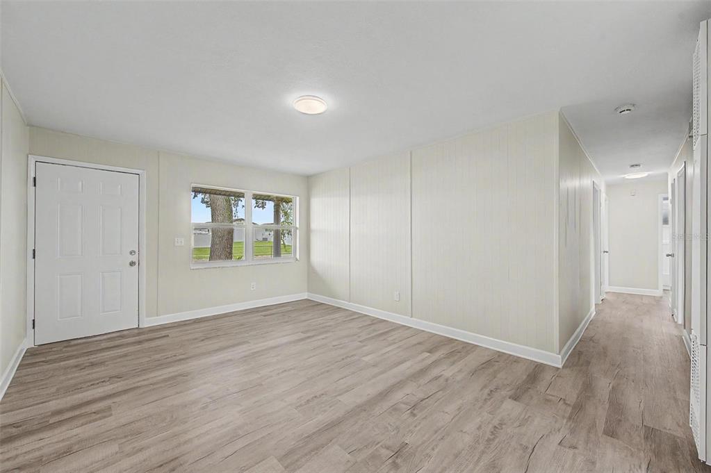 An empty room with light wood-look flooring, white paneled walls, a window, and a door — 5608 12TH AVENUE S, TAMPA, FL