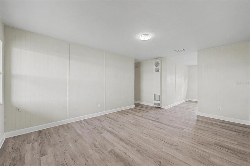 An empty room with light-colored paneled walls and wood-look laminate flooring — 5608 12TH AVENUE S, TAMPA, FL