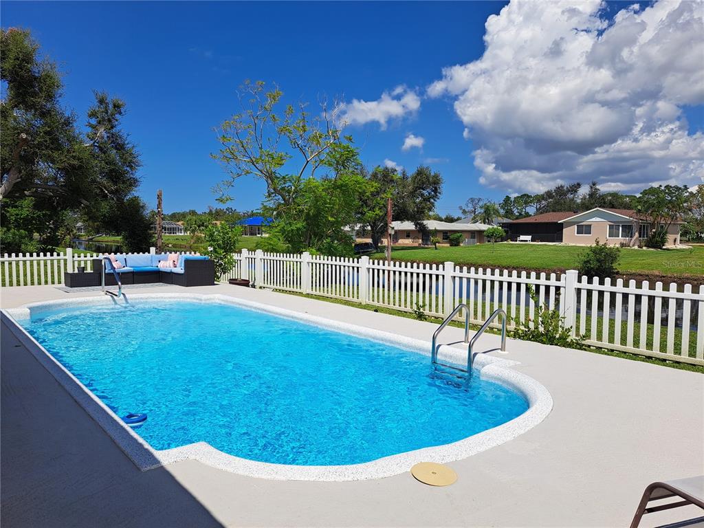 A rectangular swimming pool with a white fence sits on a patio overlooking a lawn — 231 CADDY ROAD, ROTONDA WEST, FL
