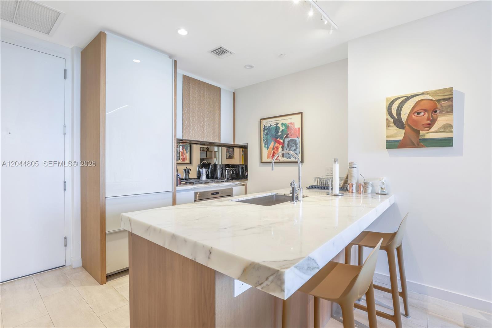 A modern kitchen features a marble-topped island, light wood cabinetry, and a white refrigerator — 2831 S Bayshore Dr # 603, Miami FL 33133, MIAMI, FL