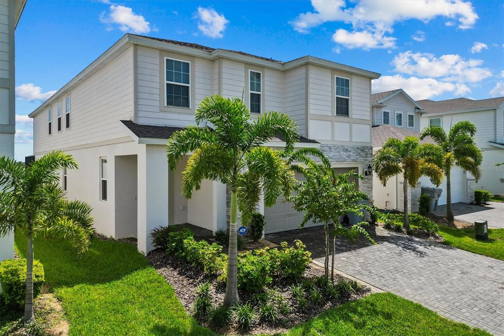 A two-story house with light siding, a stone facade, and a paved driveway with palm trees — 1697 KONA LANE, DAVENPORT, FL