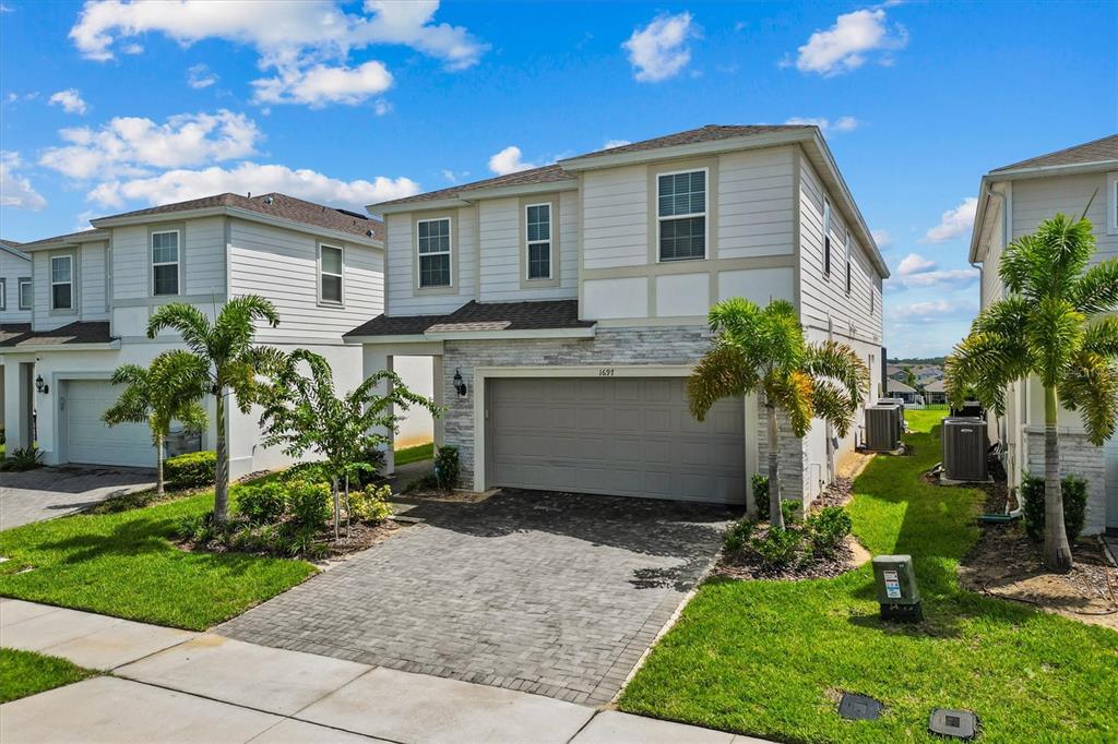A two-story house with a stone facade, gray garage door, and palm trees in front — 1697 KONA LANE, DAVENPORT, FL