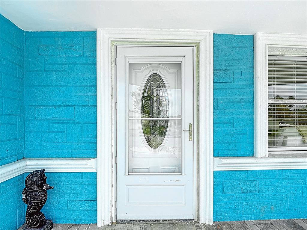 A white front door with an oval glass insert sits between bright blue brick walls — 4462 RUDDER WAY, NEW PORT RICHEY, FL
