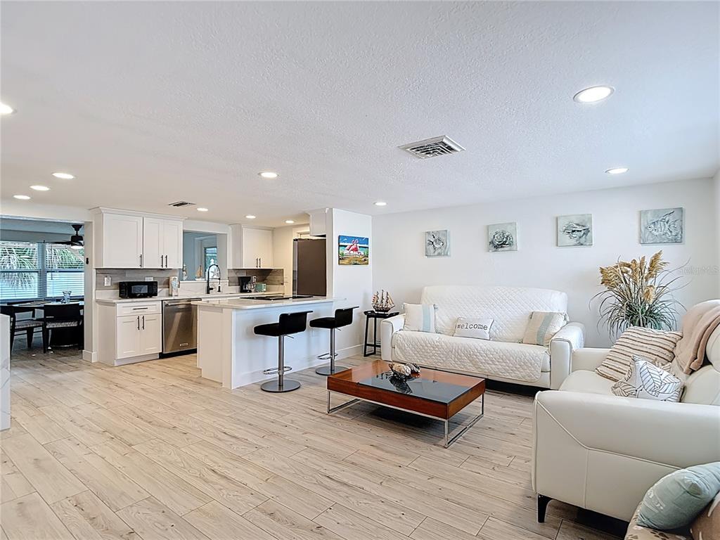 An open-concept living room and kitchen feature white cabinetry, light wood floors, and modern furniture — 4462 RUDDER WAY, NEW PORT RICHEY, FL