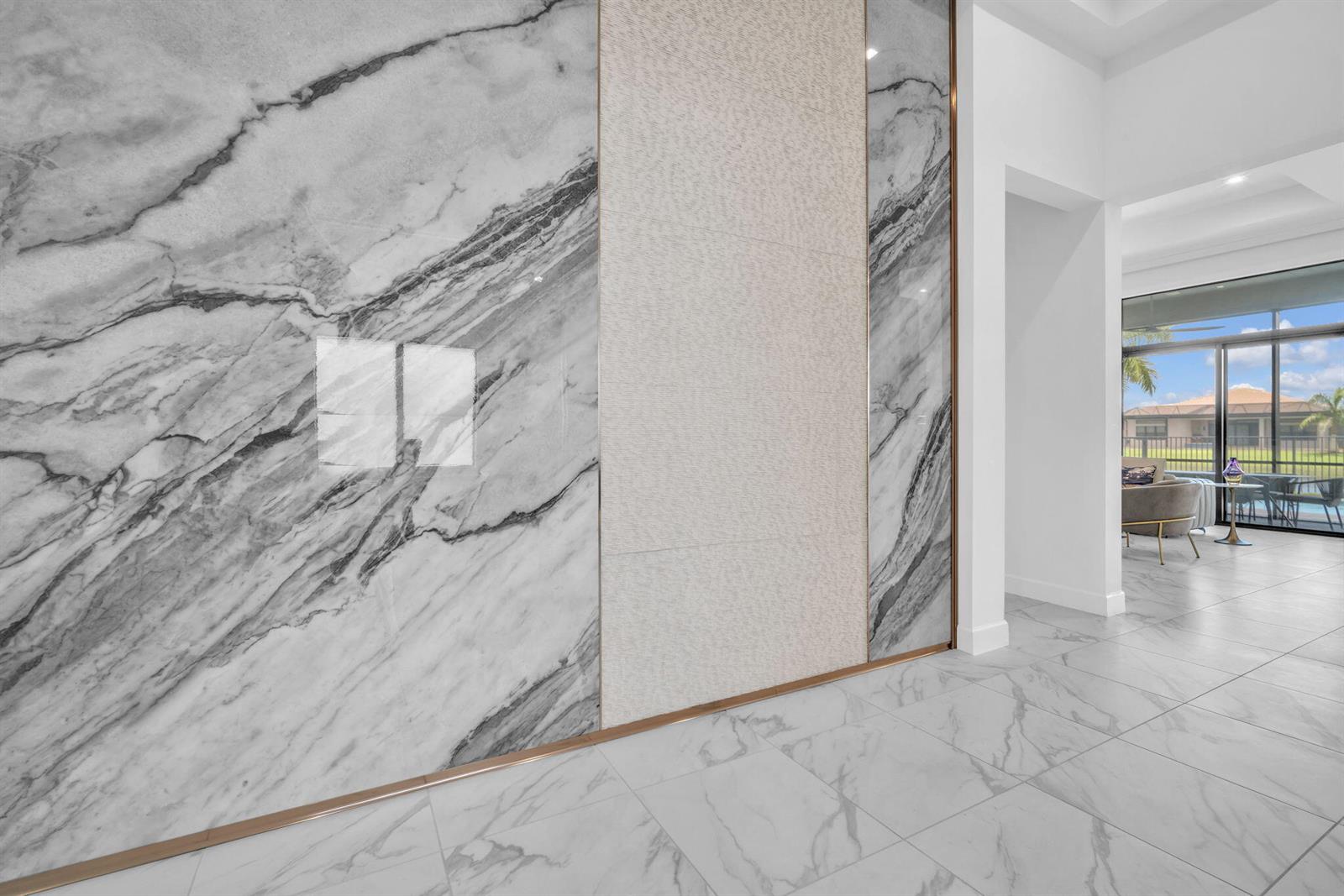 A modern interior hallway features a large marble accent wall with metallic trim and tile flooring — 9651 Spruce Woods Drive, Boynton Beach FL 33473, BOYNTON BEACH, FL