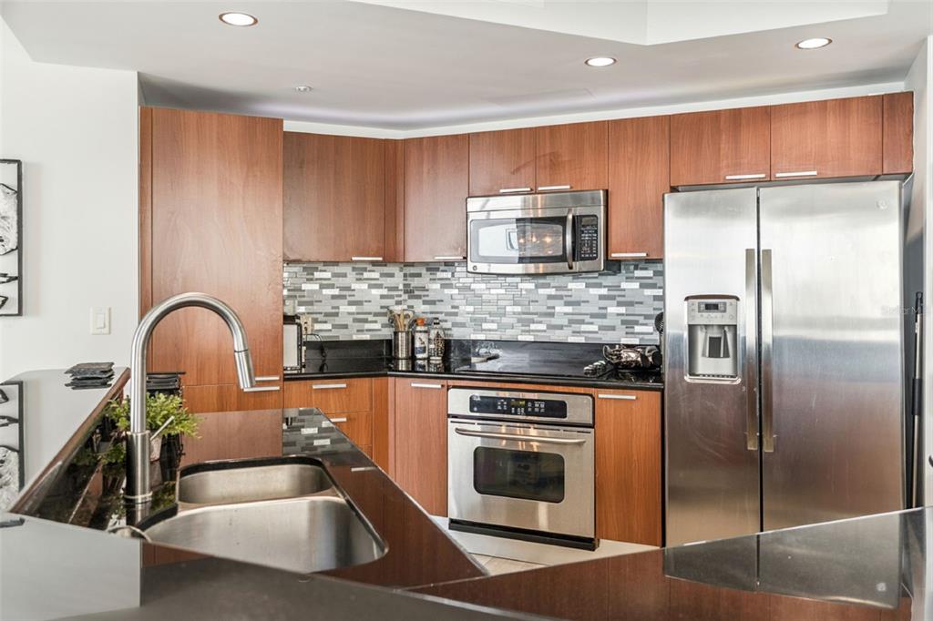 A kitchen with wood cabinets, stainless steel appliances, a black countertop, and a tiled backsplash — 231 RIVERSIDE DRIVE UNIT 702-1, HOLLY HILL, FL