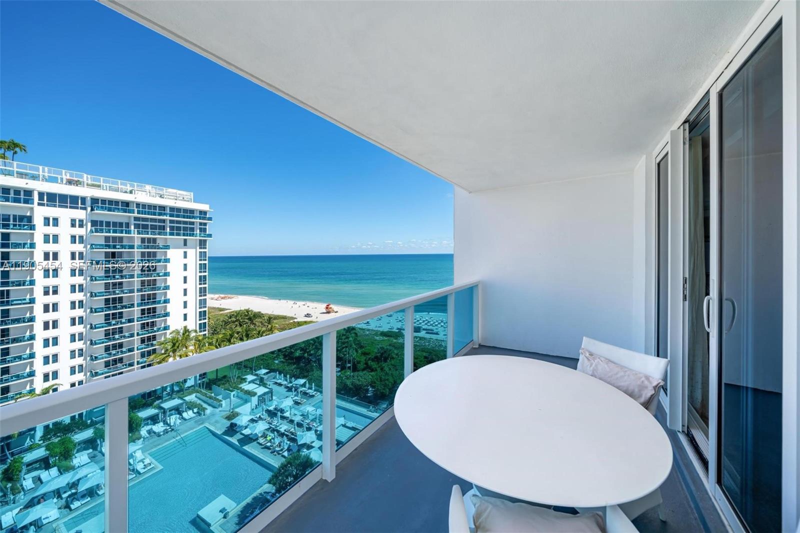 A balcony with a round table overlooks a swimming pool, beach, and the ocean — 2301 Collins Ave, Miami Beach FL 33139, MIAMI BEACH, FL