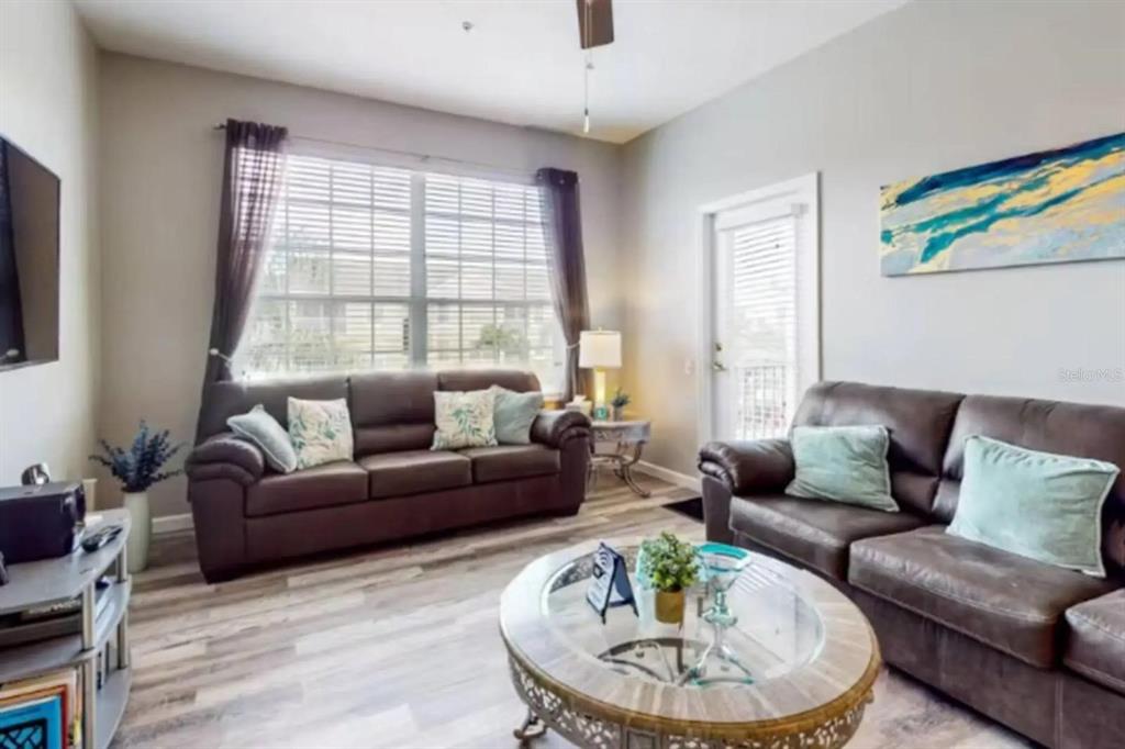 A living room features two brown leather sofas, a glass coffee table, and wood-look flooring — 2302 BUTTERFLY PALM WAY UNIT 301, KISSIMMEE, FL
