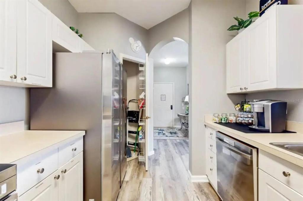 A kitchen features white cabinets, stainless steel appliances, and a doorway leading to a hallway — 2302 BUTTERFLY PALM WAY UNIT 301, KISSIMMEE, FL