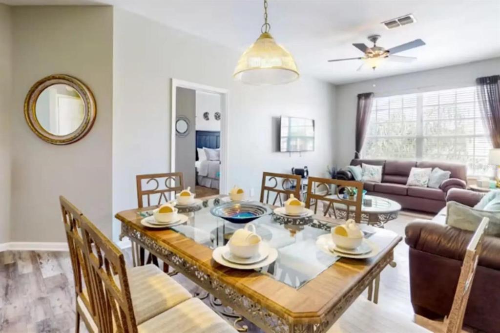 A dining area with a glass-topped table leads into a living room with brown furniture — 2302 BUTTERFLY PALM WAY UNIT 301, KISSIMMEE, FL