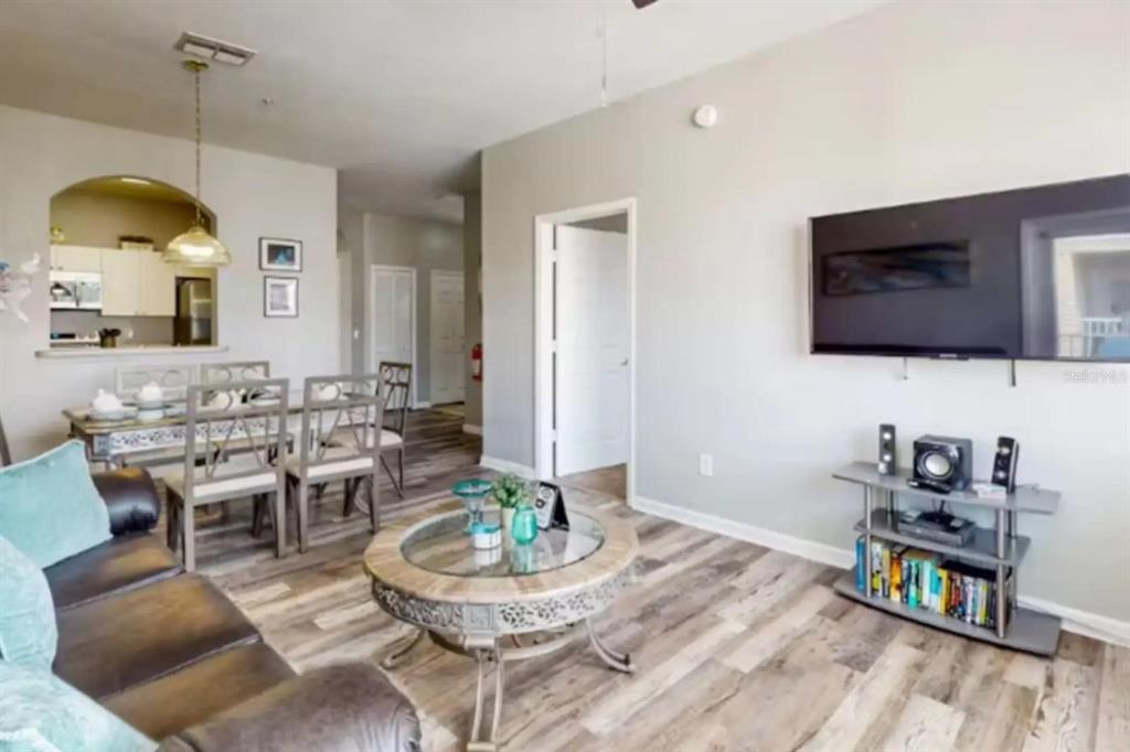 A living room with wood-look flooring, a glass coffee table, and a wall-mounted television — 2302 BUTTERFLY PALM WAY UNIT 301, KISSIMMEE, FL