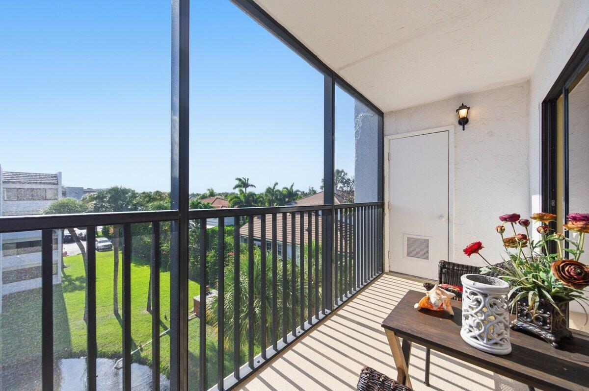 A screened-in balcony features a small table, artificial flowers, and a view of palm trees — 1605 S Us Highway 1 # A408, Jupiter FL 33477, JUPITER, FL