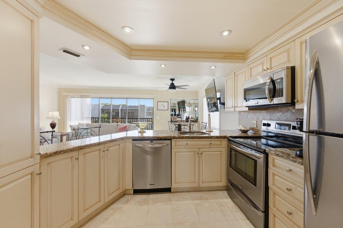 A kitchen with cream-colored cabinets, granite countertops, and stainless steel appliances opens to a living area — 1605 S Us Highway 1 # A408, Jupiter FL 33477, JUPITER, FL