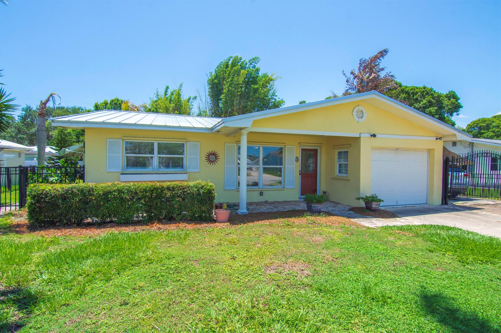 A yellow single-story house with a white garage, metal roof, and a front hedge — 475 19th Place, Vero Beach FL 32960, VERO BEACH, FL