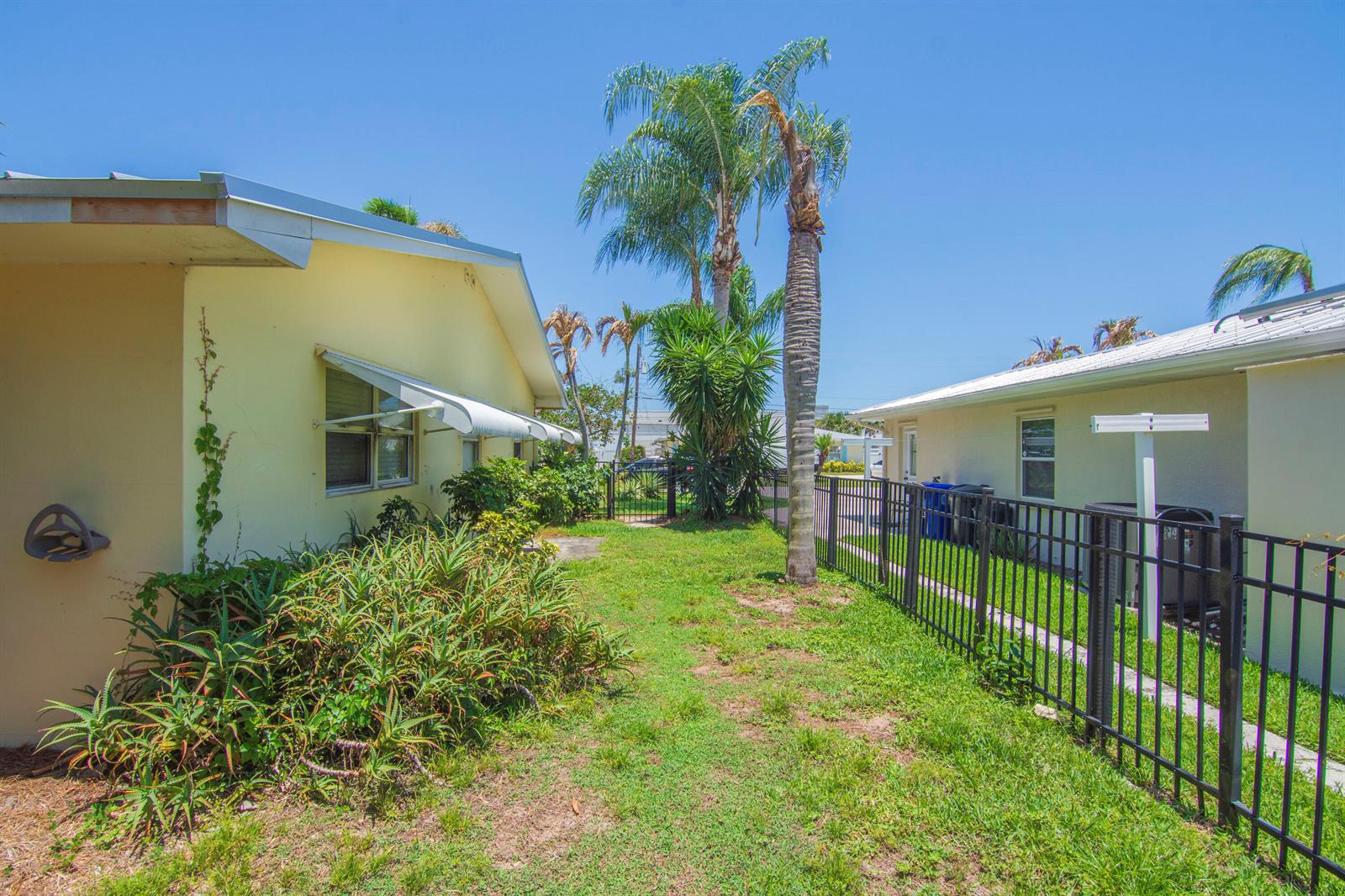 A grassy side yard sits between two yellow houses with a black metal fence — 475 19th Place, Vero Beach FL 32960, VERO BEACH, FL