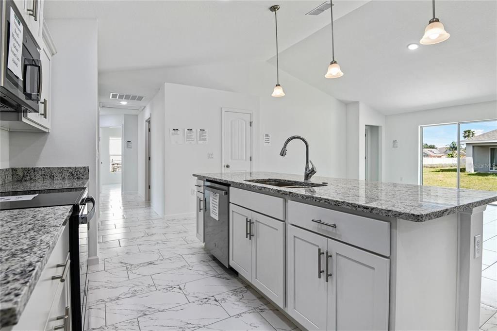 A modern kitchen features white cabinets, granite countertops, a center island, and white tiled floors — 562 MARICOPA DRIVE, KISSIMMEE, FL