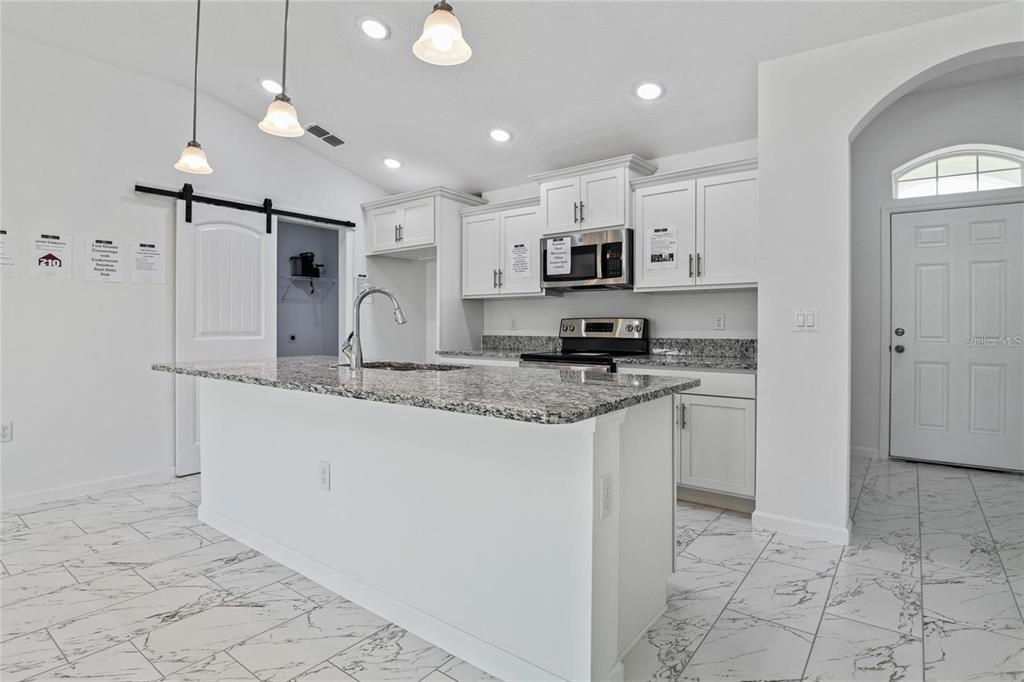 A kitchen with white cabinets, granite countertops, a center island, and white marble-look tile flooring — 562 MARICOPA DRIVE, KISSIMMEE, FL
