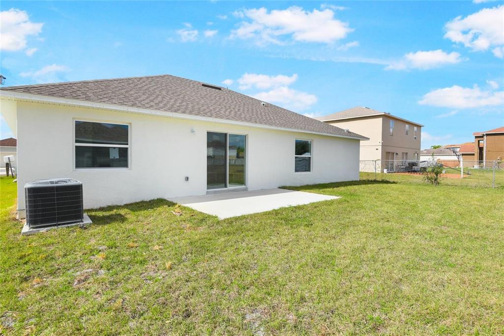 The back exterior of a white stucco house features a concrete patio and AC unit — 562 MARICOPA DRIVE, KISSIMMEE, FL