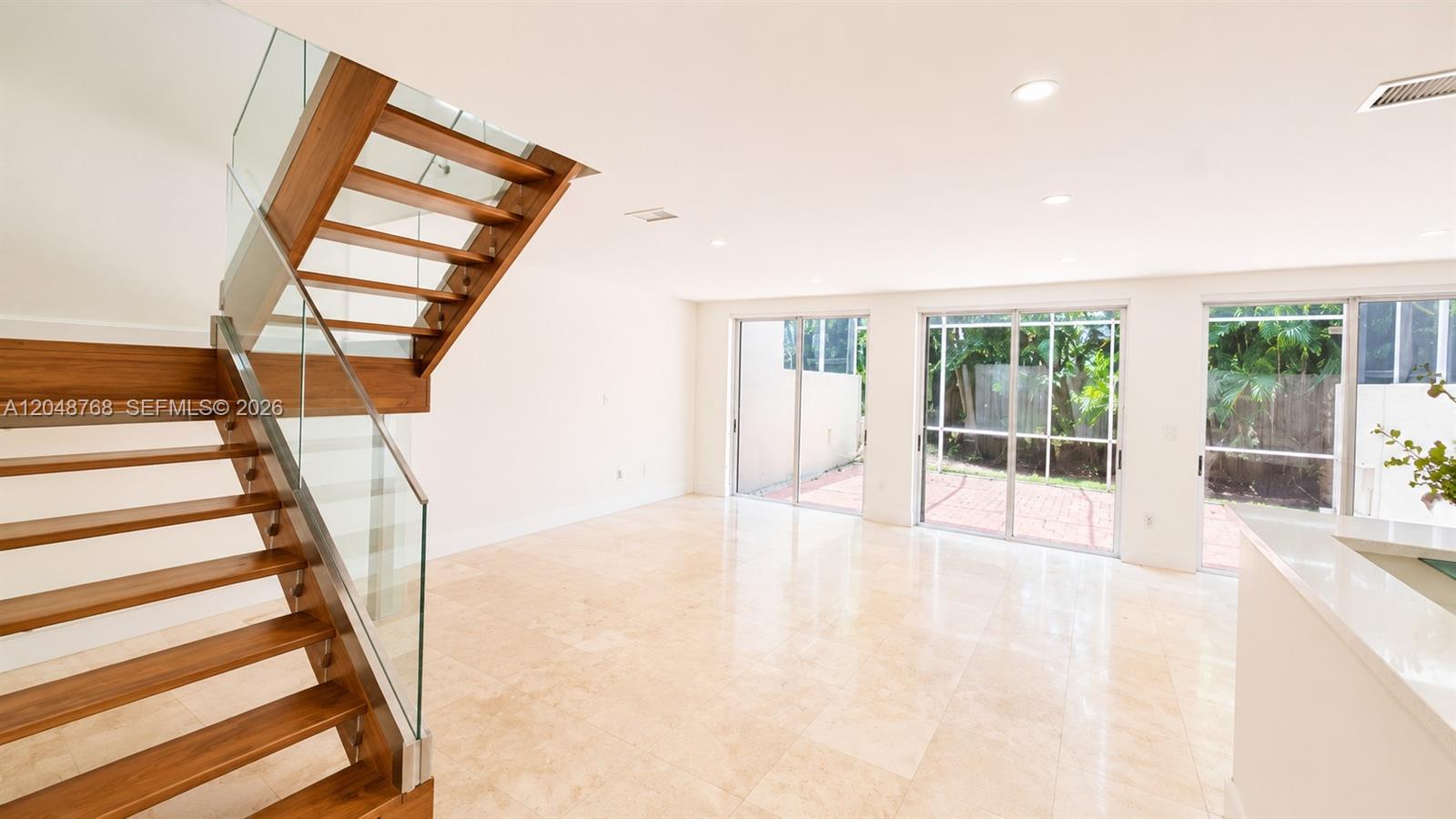 A modern living room features a wooden staircase with glass railings and tile flooring — 9805 NW 45th Ln, Doral FL 33178, DORAL, FL