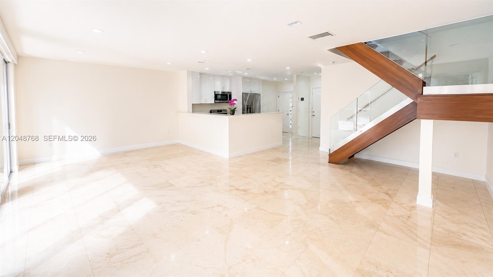 An open-concept living area features polished tile floors, a kitchen, and a modern wooden staircase — 9805 NW 45th Ln, Doral FL 33178, DORAL, FL