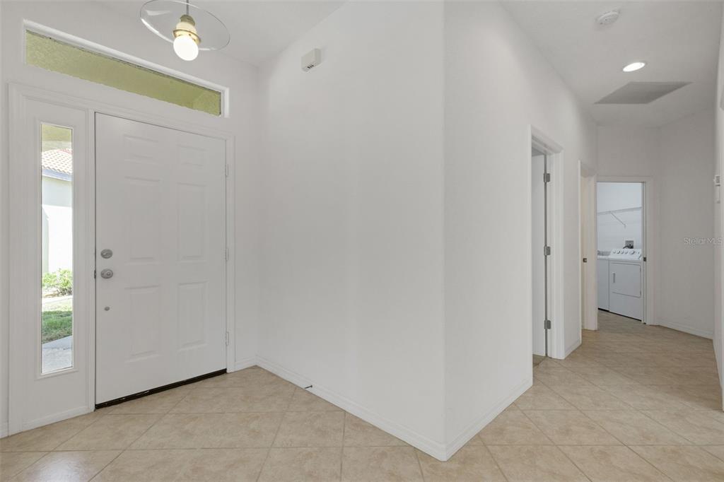 A bright entryway features white walls, tile flooring, a front door, and a laundry room — 26289 FEATHERSOUND DRIVE, PUNTA GORDA, FL