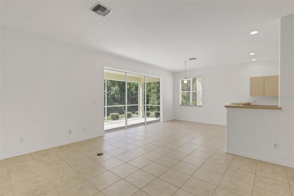 An empty living area with beige tile floors, sliding glass doors, and an open kitchen — 26289 FEATHERSOUND DRIVE, PUNTA GORDA, FL
