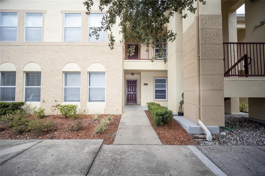 A beige two-story apartment building exterior features a central entrance with a purple door — 2814 CLUB CORTILE CIRCLE UNIT A, KISSIMMEE, FL