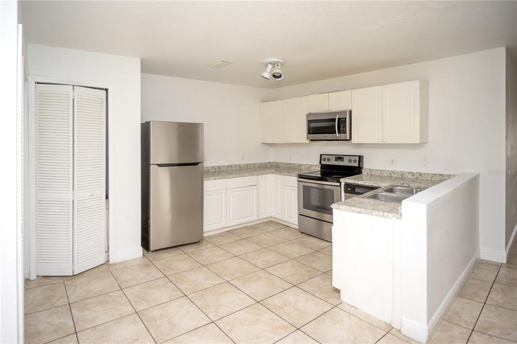 A kitchen with white cabinets, stainless steel appliances, granite countertops, and light tile flooring — 2814 CLUB CORTILE CIRCLE UNIT A, KISSIMMEE, FL