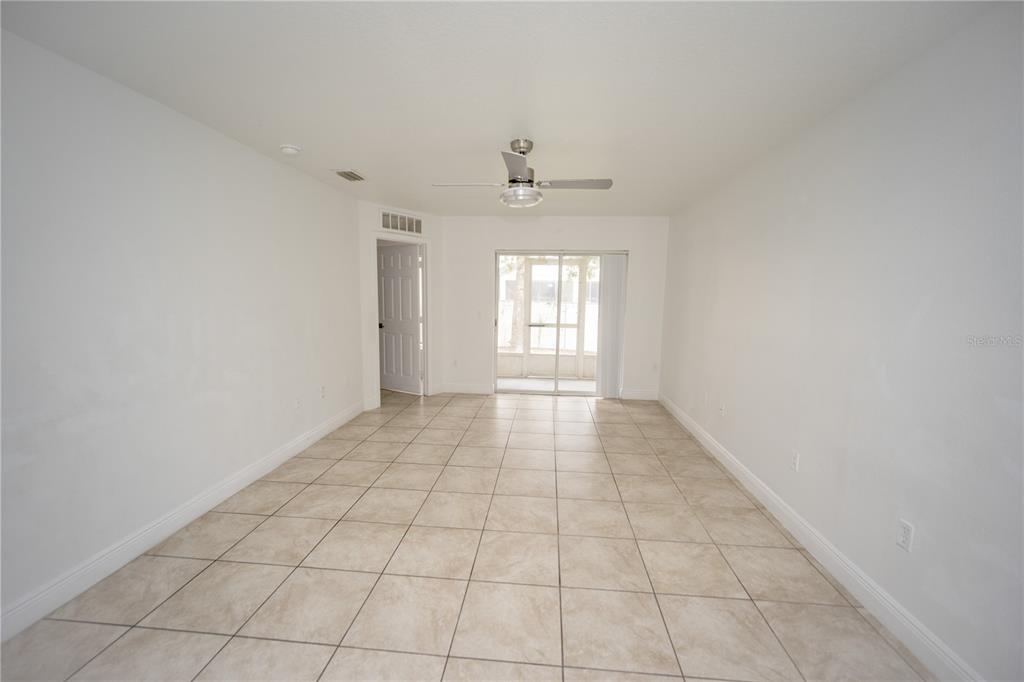An empty room features light-colored tile flooring, white walls, a ceiling fan, and sliding doors — 2814 CLUB CORTILE CIRCLE UNIT A, KISSIMMEE, FL