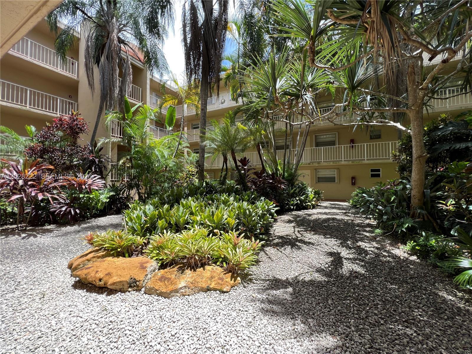 A landscaped courtyard with gravel paths and tropical plants sits between multi-story apartment buildings — 13100 SW 92nd Ave # 212, Miami FL 33176, MIAMI, FL