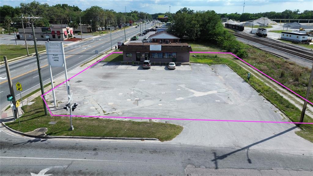 An aerial view shows a commercial building with a large paved parking lot outlined in pink — 405 S MAIN STREET, WILDWOOD, FL
