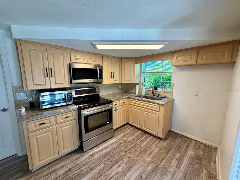 A kitchen features light wood cabinets, stainless steel appliances, and wood-look flooring — 9331 RAINBOW LANE, PORT RICHEY, FL
