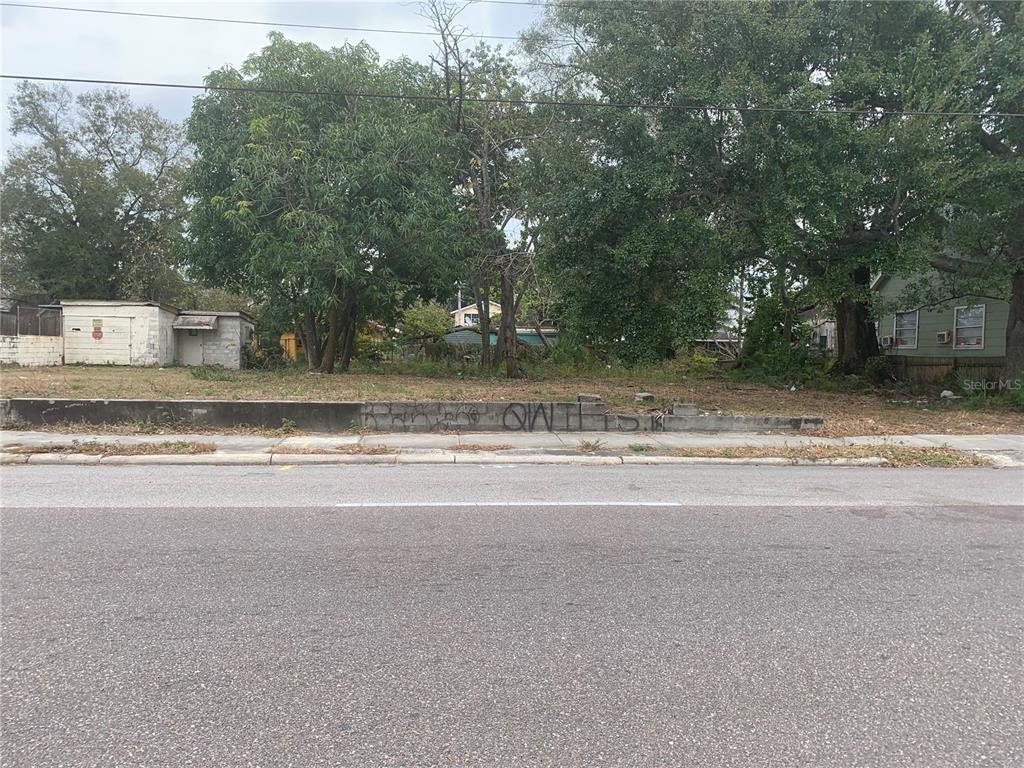 A vacant lot with a low concrete retaining wall sits beside a small white building — 3011 N 15TH STREET, TAMPA, FL