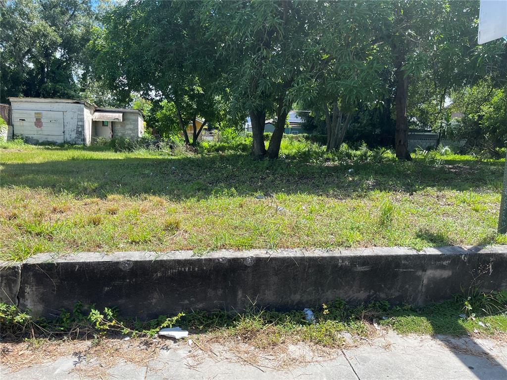 A vacant, grassy lot features a concrete retaining wall and a small detached garage — 3011 N 15TH STREET, TAMPA, FL