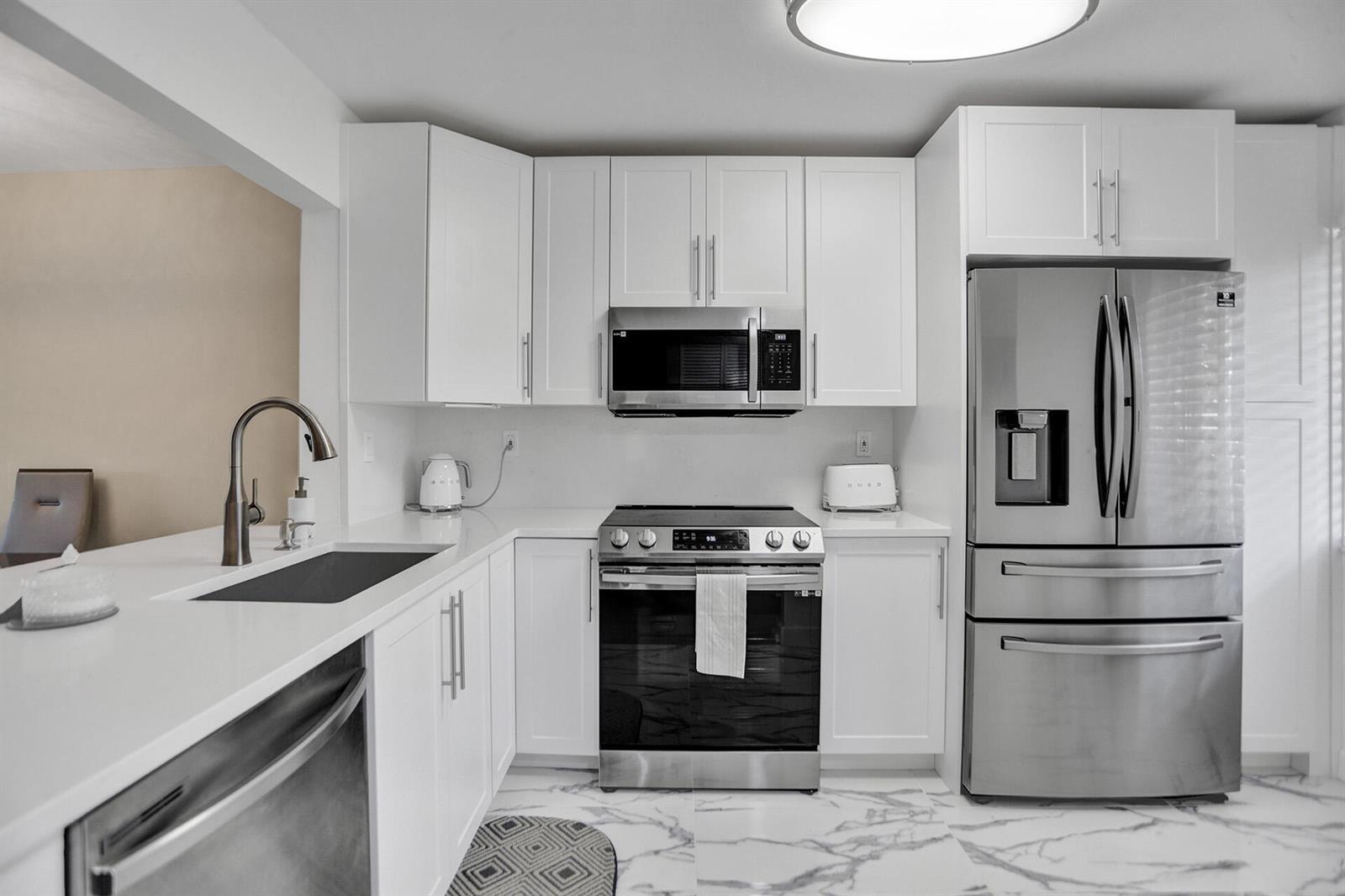 A modern kitchen features white cabinetry, stainless steel appliances, and white marble-patterned tile flooring — 3601 Inverrary Drive # 109, Lauderhill FL 33319, LAUDERHILL, FL