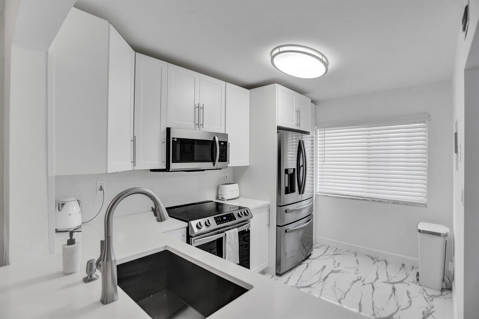 A modern kitchen features white cabinets, stainless steel appliances, and marble-patterned flooring — 3601 Inverrary Drive # 109, Lauderhill FL 33319, LAUDERHILL, FL