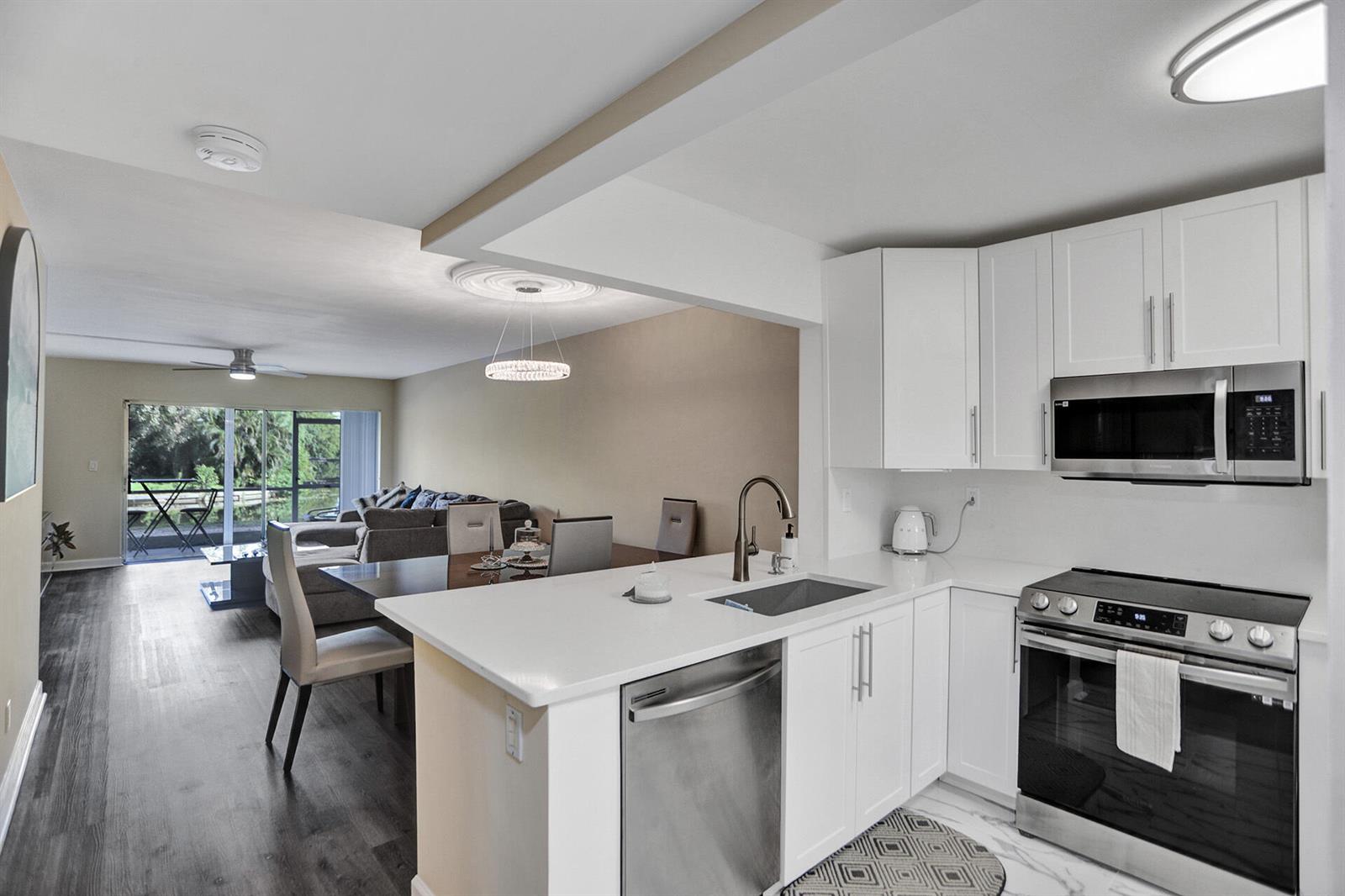 A modern kitchen with white cabinets and stainless steel appliances overlooks an open dining area — 3601 Inverrary Drive # 109, Lauderhill FL 33319, LAUDERHILL, FL
