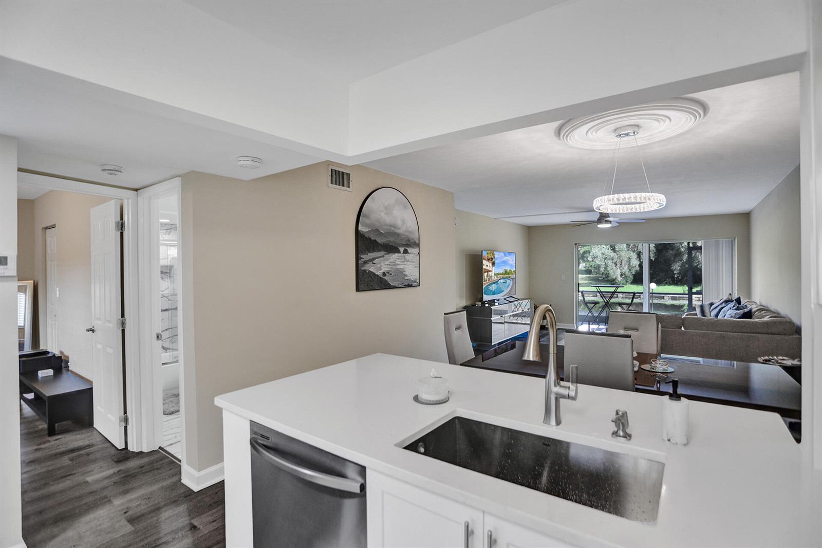 A kitchen island with a stainless steel sink overlooks an open-concept dining and living area — 3601 Inverrary Drive # 109, Lauderhill FL 33319, LAUDERHILL, FL