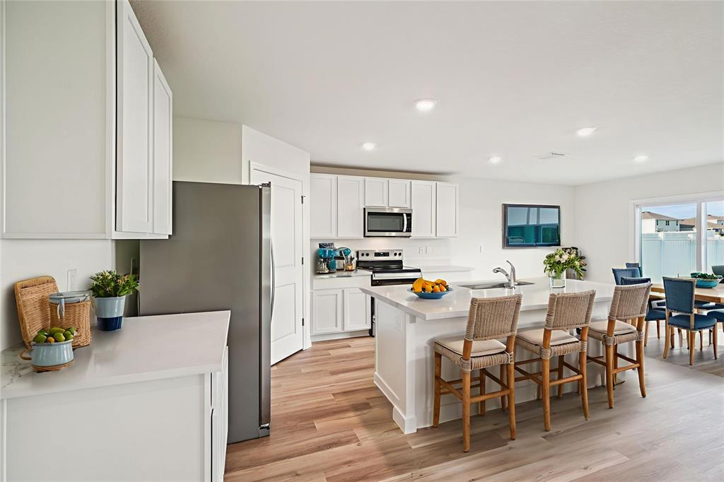 A bright kitchen features white cabinets, stainless steel appliances, a large island, and wood flooring — 8907 SW 46TH AVENUE, OCALA, FL