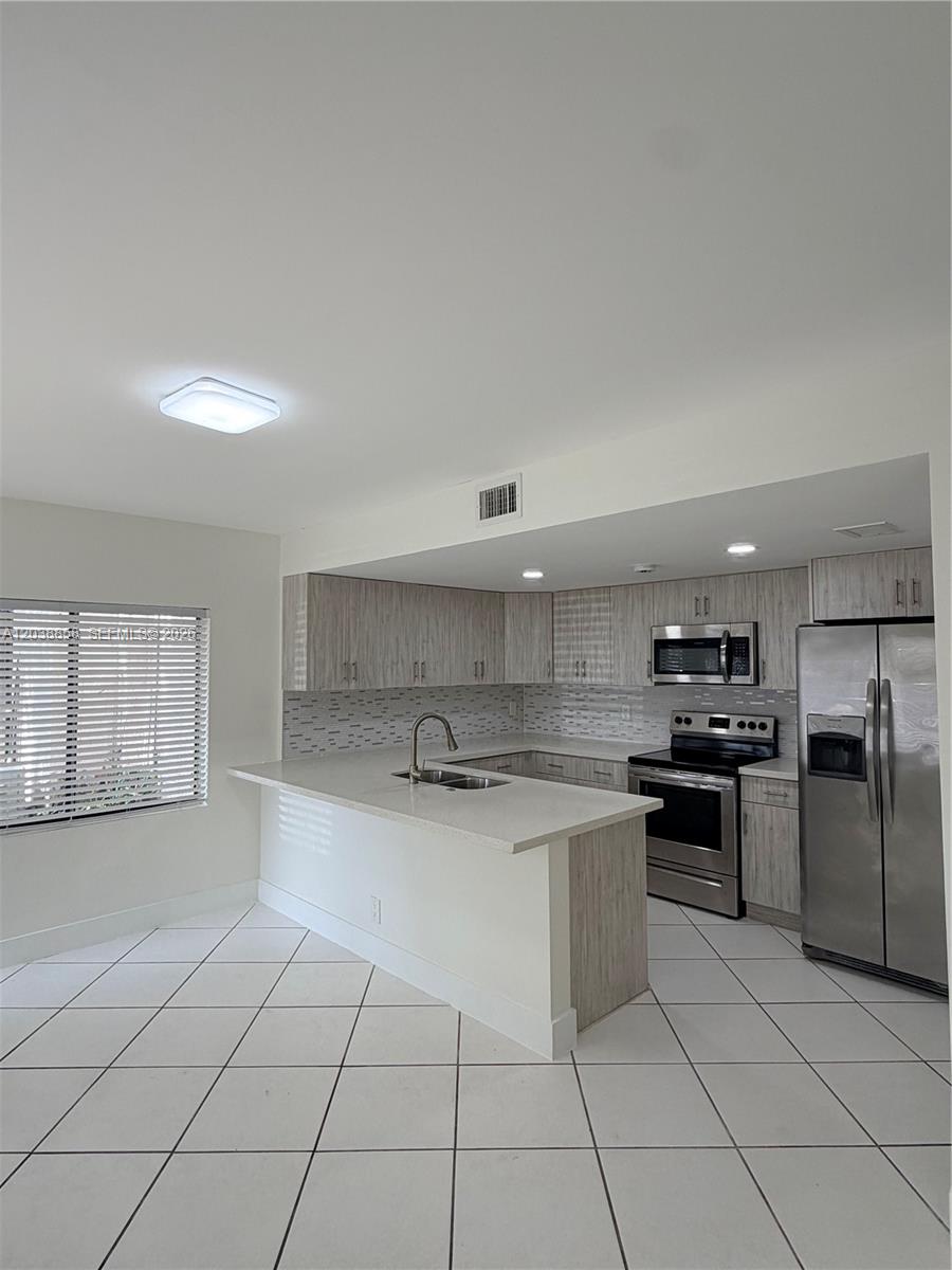 A kitchen features light wood cabinets, stainless steel appliances, and a white quartz breakfast bar — 4705 SW 62nd Ave # 104, Davie FL 33314, DAVIE, FL