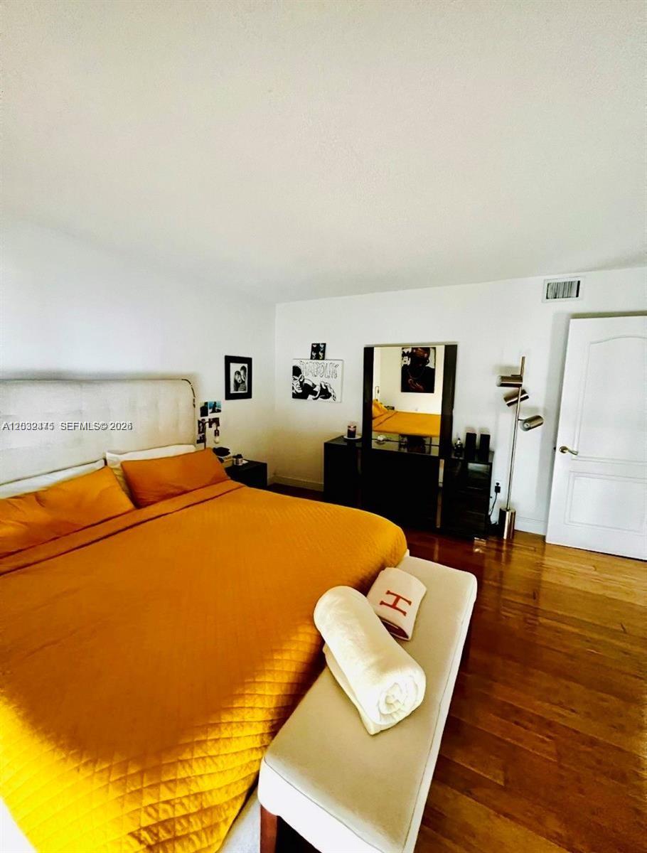 A bedroom features a mustard yellow bedspread, a white bench, and hardwood flooring — 1900 Sunset Harbour Dr # 815, Miami Beach FL 33139, MIAMI BEACH, FL
