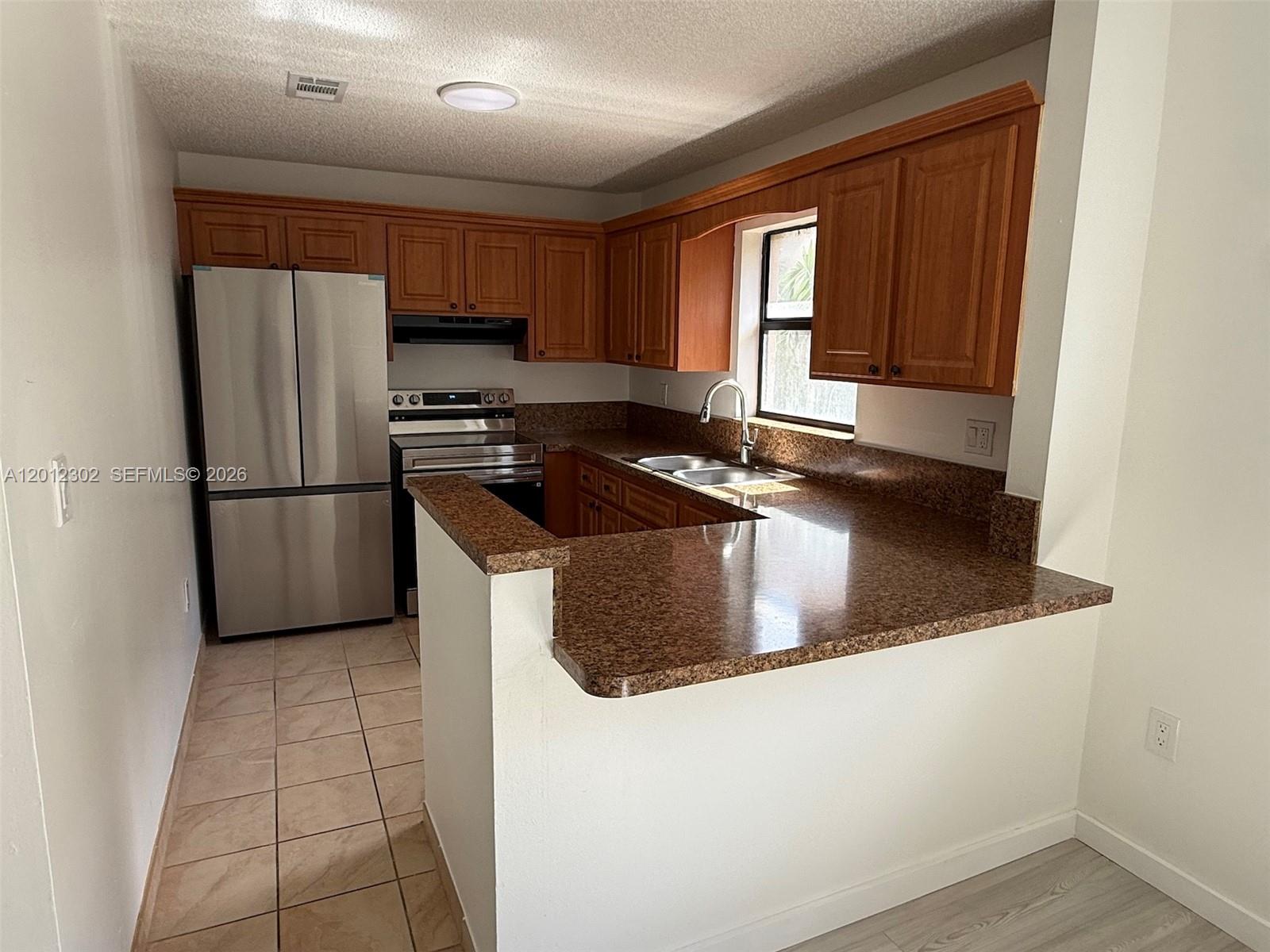 A kitchen features wood cabinets, brown granite countertops, and stainless steel appliances — 6850 NW 173rd Dr # 109, Hialeah FL 33015, HIALEAH, FL