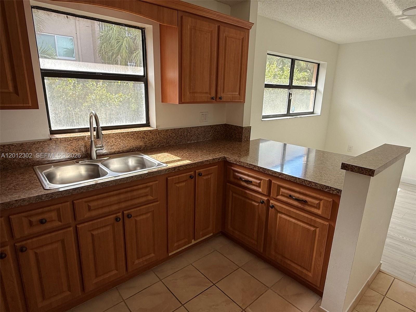 A kitchen features wood cabinets, granite countertops, a double sink, and two windows — 6850 NW 173rd Dr # 109, Hialeah FL 33015, HIALEAH, FL