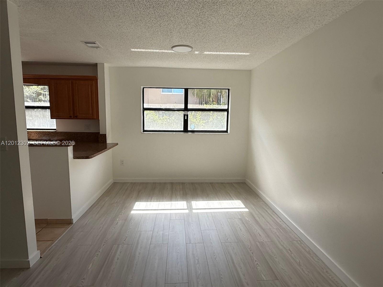 This room features light wood-look flooring, white walls, a window, and an adjacent kitchen area — 6850 NW 173rd Dr # 109, Hialeah FL 33015, HIALEAH, FL