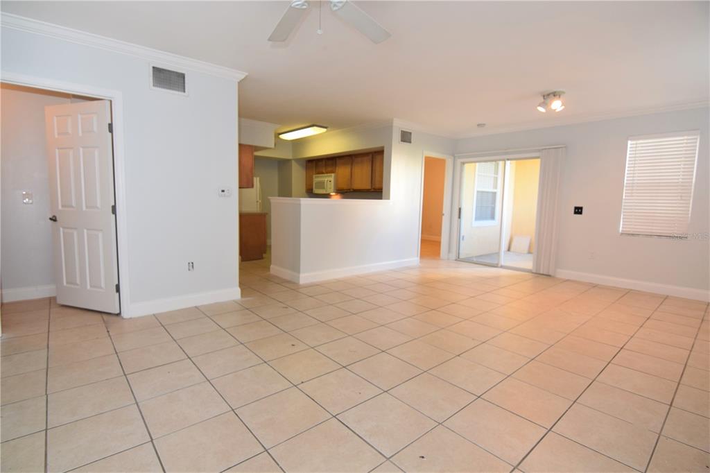 An open-concept living area features light-colored tile flooring, a kitchen with wood cabinets, and sliding doors — 1185 VILLAGIO CIRCLE UNIT 103, SARASOTA, FL