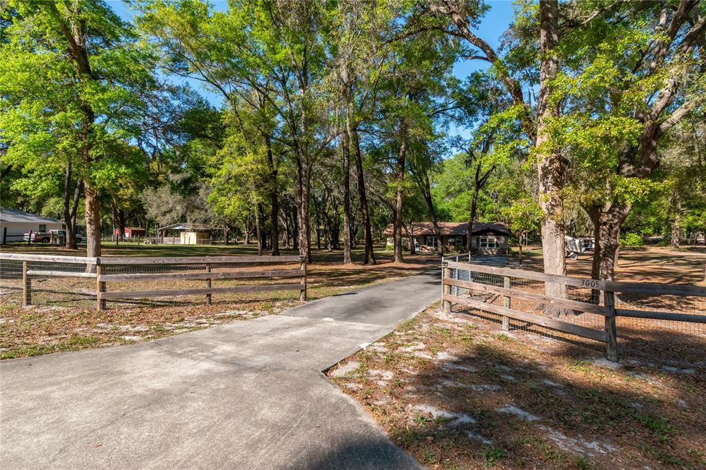 A paved driveway leads through a wooden fence toward a house surrounded by trees — 3005 SE 160TH LANE ROAD, SUMMERFIELD, FL