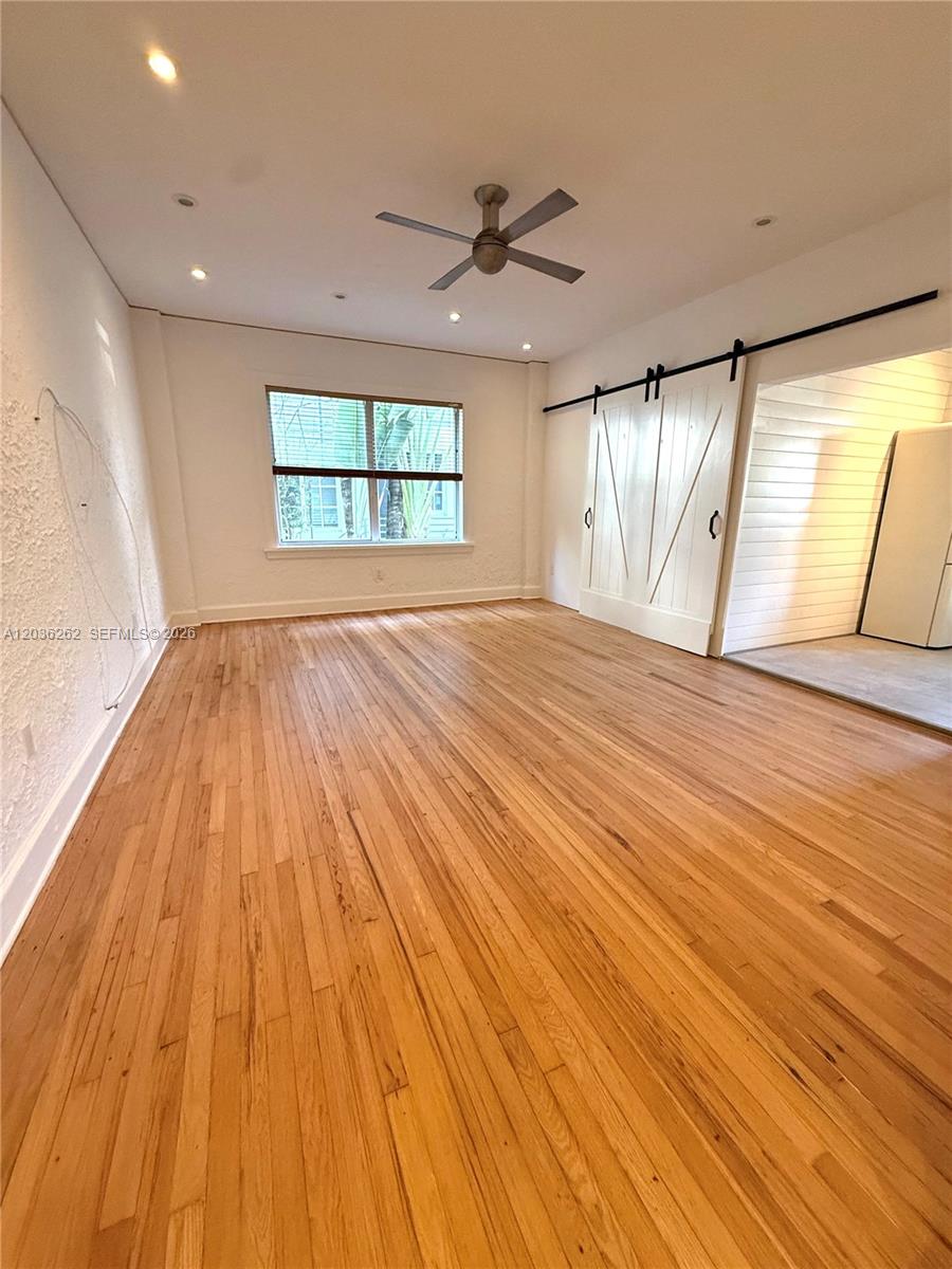 An empty room features hardwood floors, a ceiling fan, and white barn-style sliding doors — 900 16th St # 108, Miami Beach FL 33139, MIAMI BEACH, FL